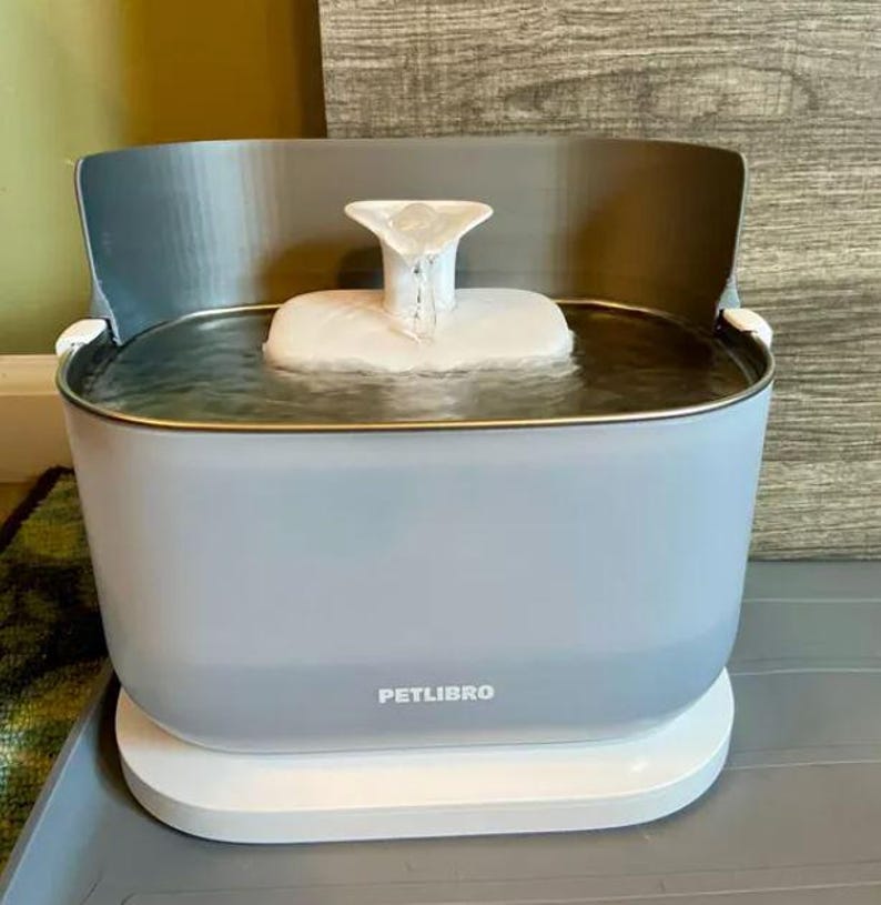 May include: A light blue PETLIBRO pet water fountain with a white base. The fountain has a water reservoir and a white, tiered water feature. The water fountain is designed for pets.