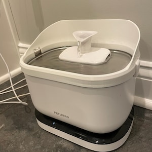 May include: A white PETLIBRO pet water fountain with a black base. The fountain has a water reservoir and a white spout with water flowing from it. The fountain is designed to provide fresh water for pets.