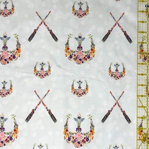 May include: A white fabric featuring a repeating pattern of floral crests and crossed wands. The crests are made of colourful flowers, and the wands have ornate handles. The background has a subtle polka dot design.
