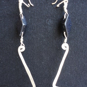 Puede incluir: Un par de pendientes de plata con un diseño geométrico. Cada pendiente tiene una pequeña piedra cuadrada de color azul oscuro.