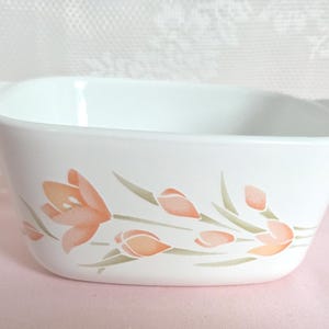 May include: White rectangular casserole dish with handles, decorated with a floral pattern of peach-colored flowers and green stems. The dish is made of ceramic and is suitable for baking and serving.