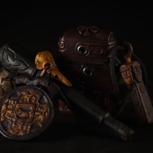 May include: A collection of antique leather goods, including a small pouch, a knife, and a decorative piece with intricate carvings. The items are arranged on a dark background.