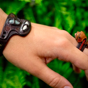 May include: A brown leather bracelet with a decorative metal design and a brown leather ring with a decorative metal design.