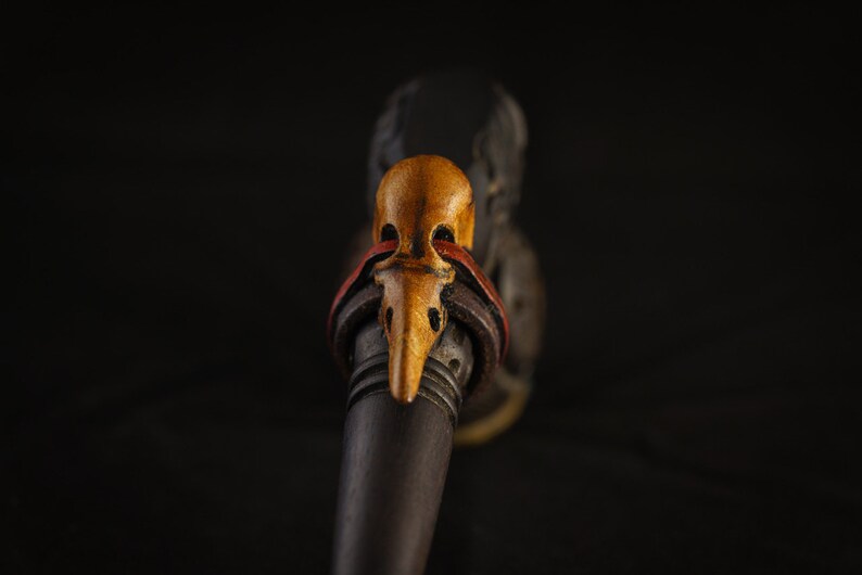 May include: A wooden pipe with a carved bird head mouthpiece. The bird head is painted in shades of yellow, orange, and red.