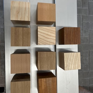 Könnte beinhalten: Zehn Holzwürfel in einem Raster angeordnet, die verschiedene natürliche Holzmaserungen und Farbtöne von hellem Beige und blassem Gelb bis hin zu mittlerem Braun und tiefem Rotbraun zeigen, jeder mit einer glatten, quadratischen Oberfläche.
