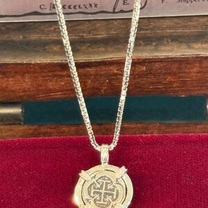 May include: A silver chain necklace with a gold-coloured pendant featuring a cross design. The pendant is surrounded by four silver accents.