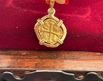 Op de afbeelding: Gouden hanger met een replica van een Spaanse gouden munt met een kruisontwerp. De hanger bevindt zich in een rode fluwelen doos.