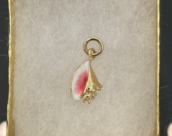 May include: A gold-colored seashell charm with white and red enamel detailing. The charm is suspended from a small gold ring and is presented in a gold box with white padding. This jewelry item is suitable for necklaces or bracelets.