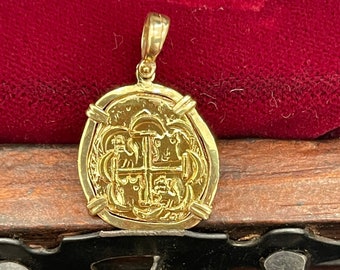 Op de afbeelding: Een gouden hanger in de vorm van een munt met een kruis en andere ontwerpen. De hanger ligt op een rode fluwelen achtergrond.