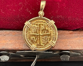 Op de afbeelding: Een gouden hanger in de vorm van een munt met een kruisontwerp en een parelrand. De hanger ligt op een rood fluwelen oppervlak.