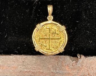 May include: A gold-colored pendant in the shape of a coin with a cross design and intricate details. The pendant is in a wooden box with a black velvet lining.