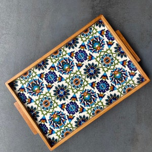 May include: A wooden serving tray with a decorative tile design. The tile features a repeating pattern of blue, green, and orange floral motifs on a white background.