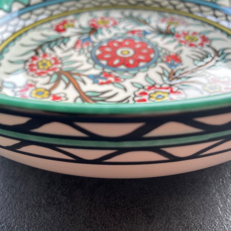 Puede incluir: Un cuenco de cer&aacute;mica blanca con un patr&oacute;n geom&eacute;trico verde, negro y blanco alrededor del borde. El cuenco est&aacute; decorado con un dise&ntilde;o floral en tonos rojos, azules, amarillos y verdes.