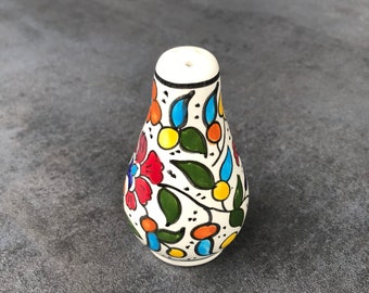 May include: White ceramic salt or pepper shaker with a floral design in shades of red, blue, yellow, and green.