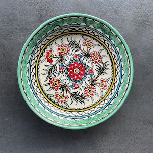 Puede incluir: Un cuenco de cer&aacute;mica verde con un centro blanco que presenta un dise&ntilde;o floral en rojo, azul y amarillo. El cuenco tiene un borde decorativo con acentos verdes y blancos.