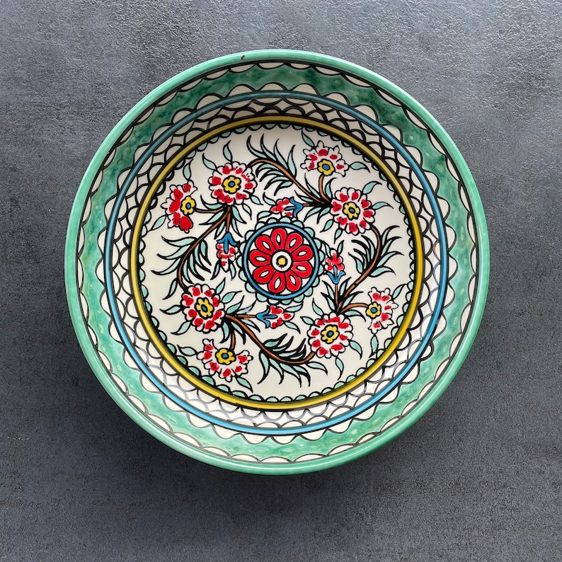 Puede incluir: Un cuenco de cer&aacute;mica verde con un centro blanco que presenta un dise&ntilde;o floral en rojo, azul y amarillo. El cuenco tiene un borde decorativo con acentos verdes y blancos.