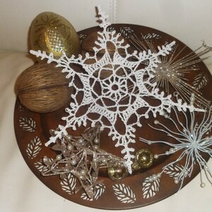 May include: A white crocheted snowflake ornament on a brown metal tray decorated with gold and white star ornaments and other decorative elements.