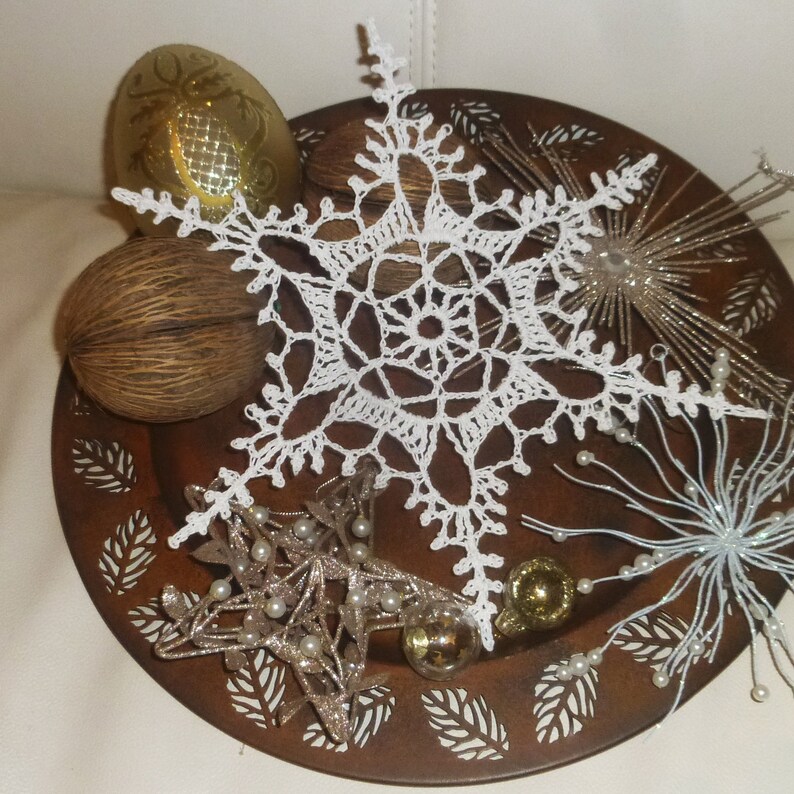 May include: A white crocheted snowflake ornament on a brown metal tray decorated with gold and white star ornaments and other decorative elements.