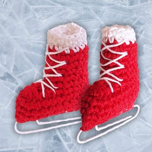 May include: A pair of red crocheted ice skates with white laces and trim. The skates have a white blade and are set against a light blue background with a cracked ice pattern. The skates are a festive decoration.