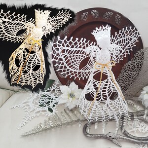 May include: Two crocheted angels, one white and one cream, with delicate lace detailing. Both angels have a crown and a bow made of twine.