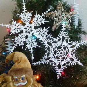 May include: White crocheted snowflakes hanging on a Christmas tree with a gold star ornament and a Santa Claus figurine at the bottom.