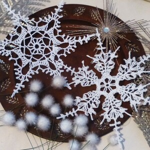 May include: Two white crocheted snowflakes on a brown wooden plate with white fluffy decorations.