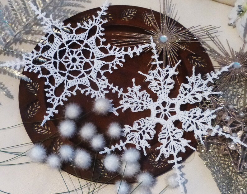 May include: Two white crocheted snowflakes on a brown wooden plate with white fluffy decorations.