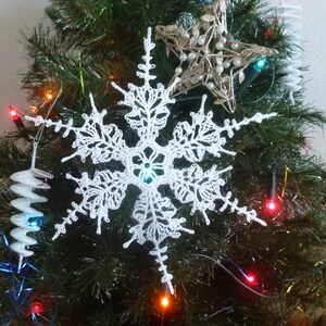 May include: A white crocheted snowflake ornament hanging on a Christmas tree with colourful lights.