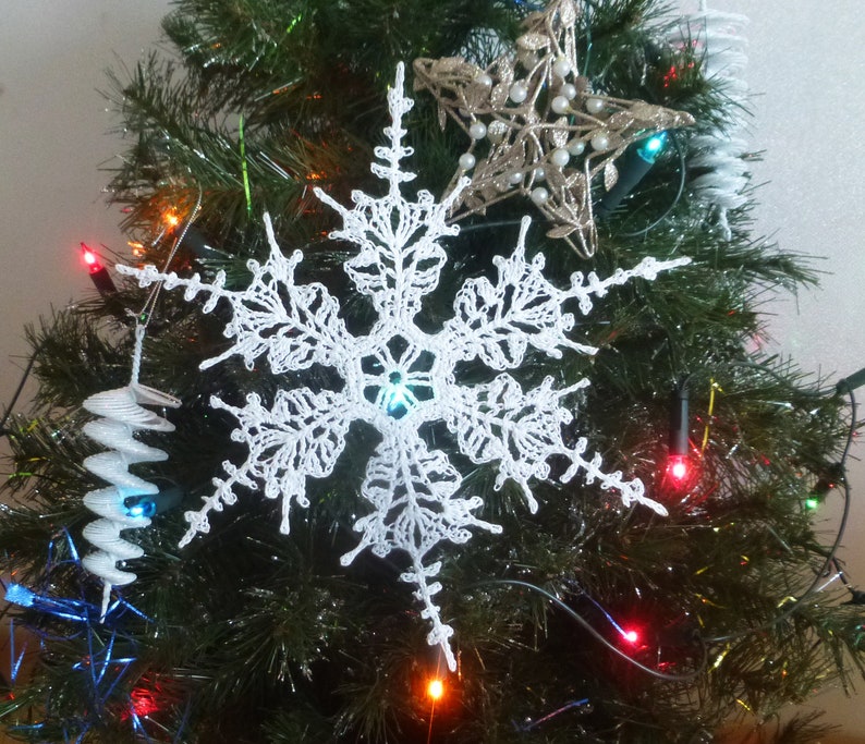 May include: A white crocheted snowflake ornament hanging on a Christmas tree with colourful lights.