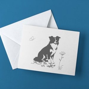 May include: A white greeting card with a gray illustration of a Border Collie dog, a butterfly, and a flower. The card is accompanied by a white envelope. The background is a solid blue.