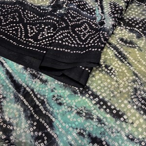 Puede incluir: Primer plano de una tela con un patrón único. La tela presenta una mezcla de tonos negros, verde azulado y verde oliva. El diseño incluye pequeños patrones cuadrados blancos dispuestos en filas y rayas diagonales, creando una apariencia texturizada.