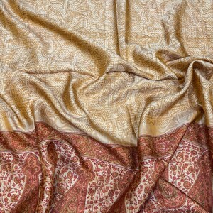 Könnte beinhalten: Ein drapierter Stoff mit einem cremefarbenen geometrischen Muster oben und einem detaillierten Paisley-Bordürenrand in Rot- und Brauntönen unten. Der Stoff hat einen seidigen Glanz.