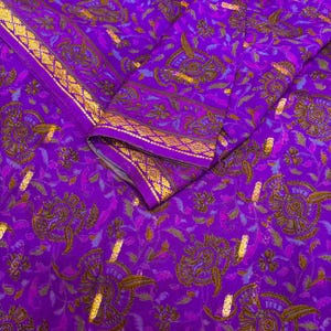 Può includere: Un tessuto viola vibrante con un intricato motivo floreale e dettagli dorati. Il design presenta fiori e foglie stilizzati, con un bordo dorato. Il tessuto è piegato, mostrando il design dettagliato.