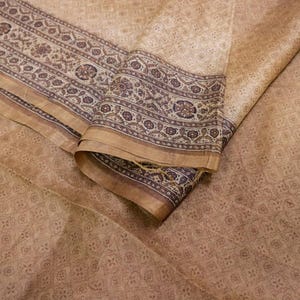 Könnte beinhalten: Ein gefaltetes Textil mit einem sich wiederholenden geometrischen Muster in Beige- und Brauntönen. Der Rand hat ein detailliertes Blumendesign in Dunkelbraun und Beige. Der Stoff scheint Seide oder ein ähnliches leichtes Material zu sein.