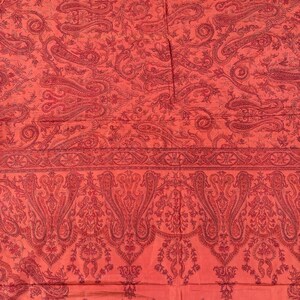 May include: A close-up of a red textile with a paisley pattern. The fabric features a repeating design of curved, teardrop-shaped motifs in a darker shade of red. The overall effect is a rich, detailed, and ornate design.