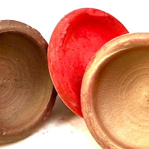 May include: Three terracotta bowls, one red, one brown and one gold. The bowls are round and have a slight lip around the edge.
