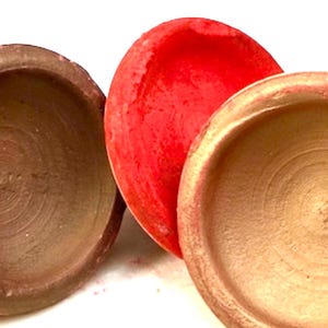 May include: Three terracotta bowls, one red, one brown and one gold. The bowls are round and have a slight lip around the edge.