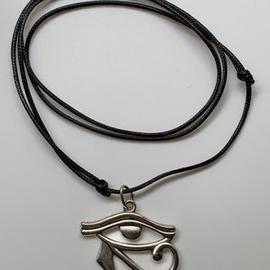 May include: A silver Eye of Horus pendant on a black cord necklace.