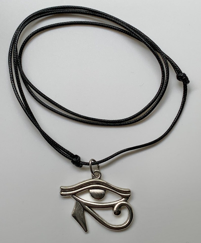 May include: A silver Eye of Horus pendant on a black cord necklace.