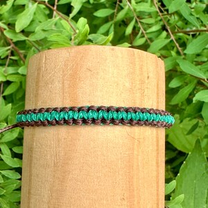 May include: A green and brown friendship bracelet made with woven string.