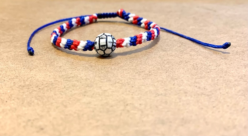 May include: A blue, white, and red braided bracelet with a white and black soccer ball charm.
