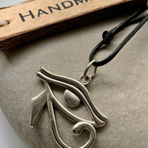 May include: A silver Eye of Horus pendant necklace on a black cord. The pendant is a detailed representation of the ancient Egyptian symbol. The necklace is handmade.