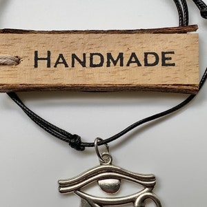 May include: A black cord necklace with a silver Eye of Horus pendant. The necklace has a wooden tag that says "HANDMADE".