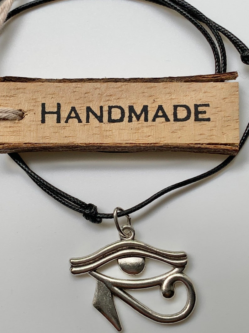 May include: A black cord necklace with a silver Eye of Horus pendant. The necklace has a wooden tag that says "HANDMADE".