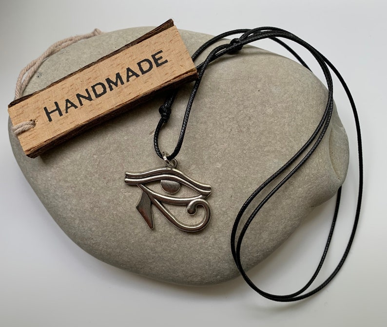 May include: A silver Eye of Horus pendant necklace on a black cord with a wooden tag that says "HANDMADE".