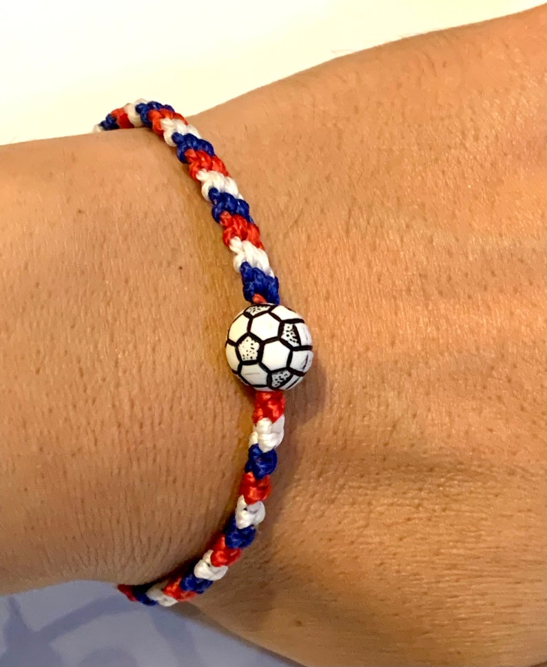 May include: A red, white, and blue braided bracelet with a black and white soccer ball charm.