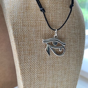 May include: Silver Eye of Horus pendant necklace on a black cord. The pendant is a detailed representation of the ancient Egyptian symbol.