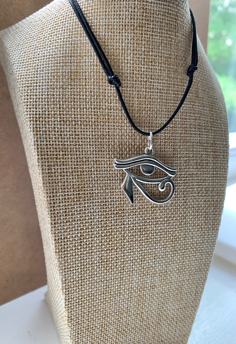 May include: Silver Eye of Horus pendant necklace on a black cord. The pendant is a detailed representation of the ancient Egyptian symbol.