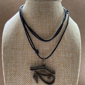 May include: A black cord necklace with a bronze pendant featuring the Eye of Horus symbol.