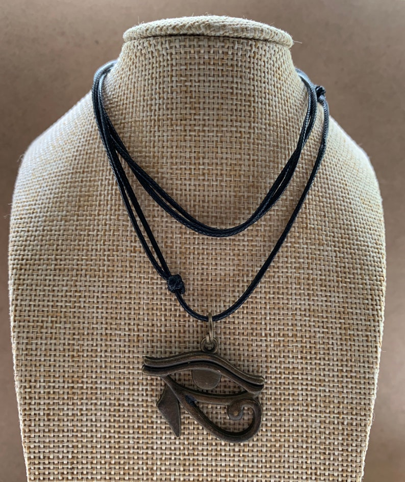 May include: A black cord necklace with a bronze pendant featuring the Eye of Horus symbol.